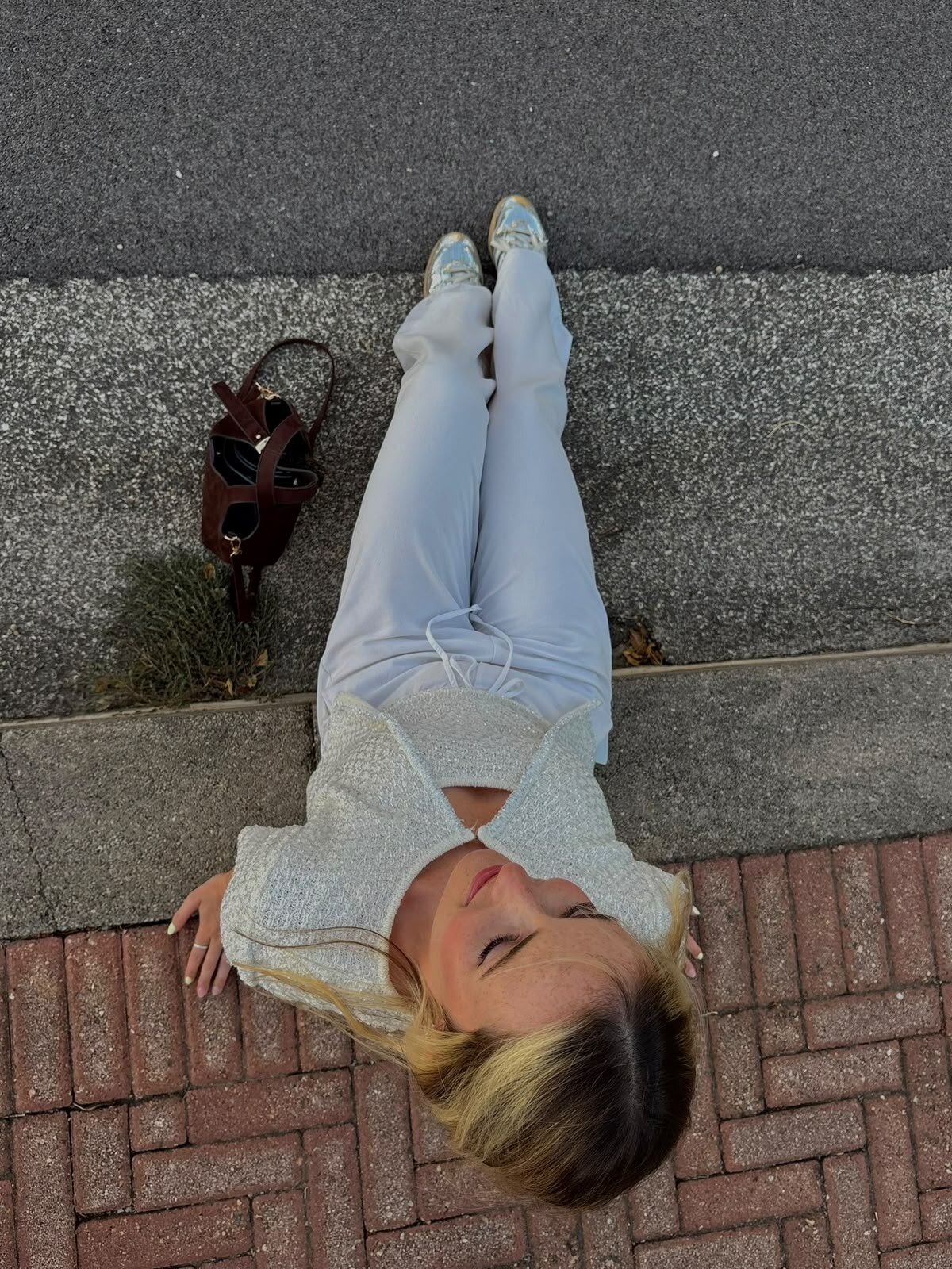 Léna allongée sur un trottoir, tenue claire photographiée en plongée.
