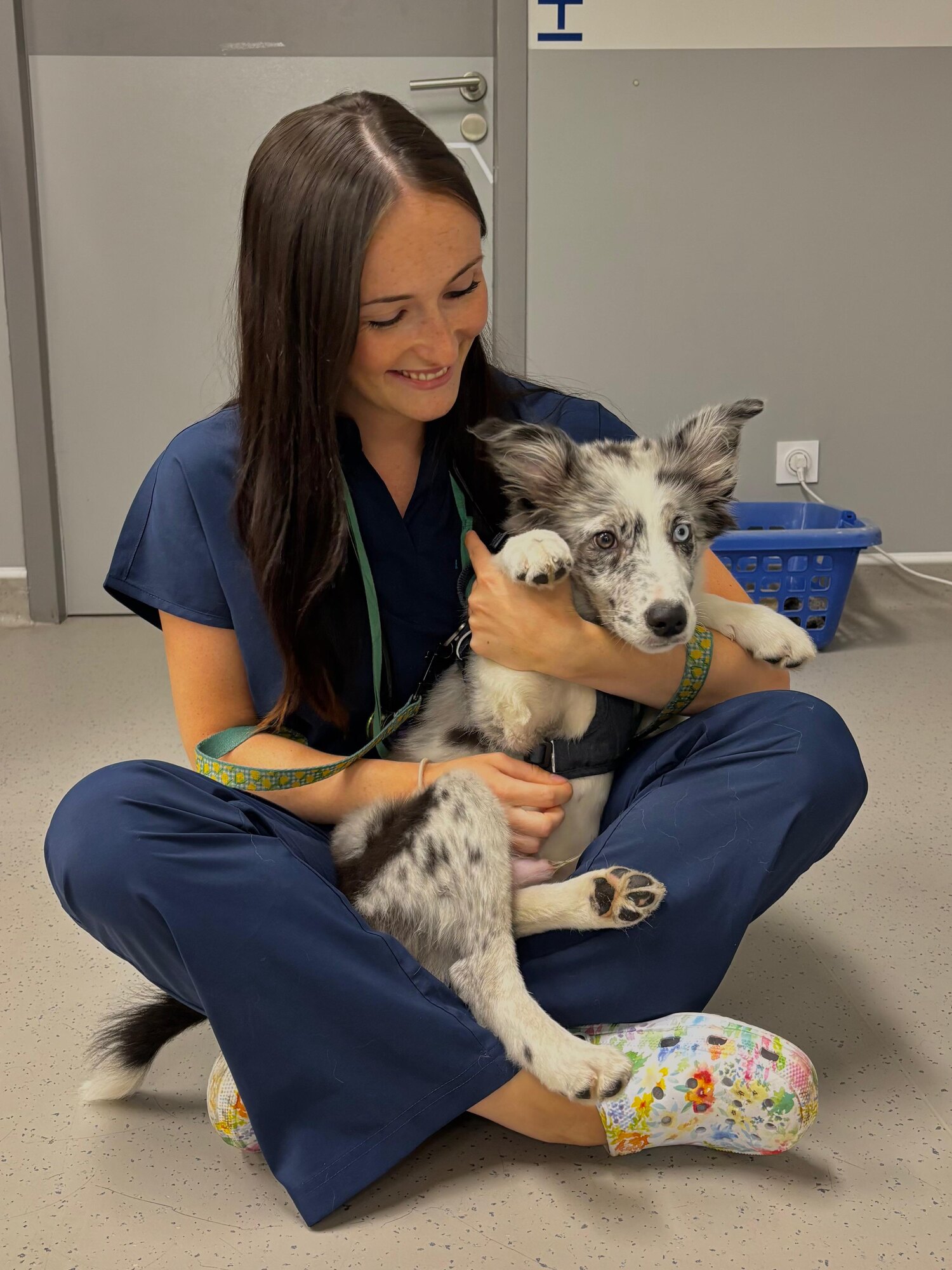 Étudiante en tenue vétérinaire assise au sol avec un chiot dans les bras.